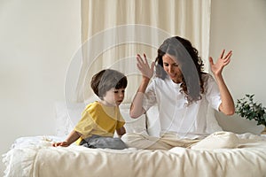Young mother reading fairytales to little kid sitting on bed in bedroom entertain child on holiday