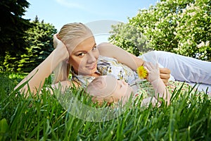 Young mother reclines on green grass next to her baby