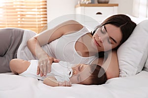 Young mother resting near her sleeping baby on bed at home