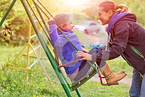 Young Mother Riding Little Daughter on Seesaw in Spring Park