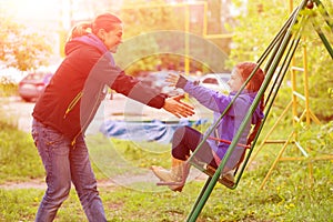 Young Mother Riding Little Daughter on Seesaw in Spring Park