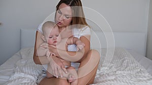 A young mother rocks the baby in her arms. The baby cries and does not want to sleep.