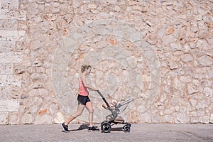 Young mother running with the stroller of her baby to stay in shape after childbirth