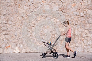 Young mother running with the stroller of her baby to stay in shape after childbirth