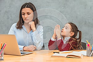 Young mother and schoolgirl on a gray background. My daughter hands up asking my mother to look at the laptop. During