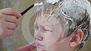 Young mother shaves head of blond boy with razor for preventing pediculosis. Good family tradition