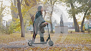 Young mother showing her toddler son how to ride a scooter in a autumn park. Active family leisure. Training, sports