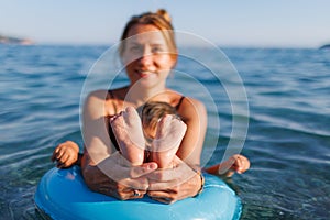 A young mother shows the legs and arms of her baby, who is sitting in an inflatable ring in the sea