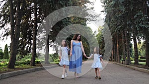 Young mother with siblings daughters together walking towards sun having fun in city botanical garden. Motherhood