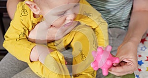 A young mother sits on the bed with a small child in her arms and controls the game with a teether and other tactile