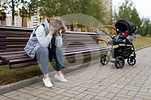 a young mother sits on a bench upset next to a baby stroller, Concept of postpartum depression