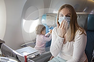 A young mother is sitting in an airplane chair in a medical respiratory mask with a scared face loking in camera. concept covid-19