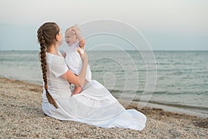 Young mother sitting on beach and holding baby. Joys of motherhood photo