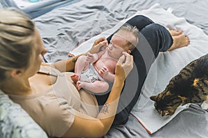 Young mother sitting on a bed, holding her newborn son with cute brown hair on her lap, communicating with him. Big