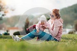 A young mother is sitting on the grass, playing with her baby. Recreation in the park with a child. Blurred background. Children`