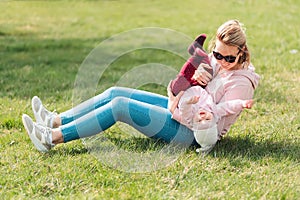 A young mother is sitting on the grass, playing with her baby. Recreation in the park with a child. Top view. Children`s day