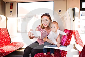 Young mother with smartphone travelling with baby by train.