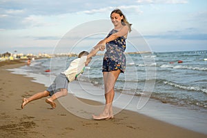 Young mother and smiling baby boy son playing on the beach on the Sunset. Positive human emotions, feelings, joy. Funny cute child