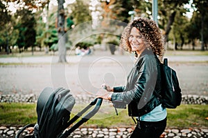 Young mother smiling walking with baby carriage in park. Details of motherhood