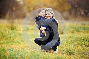 Young mother and son in autumn forest park, yellow foliage. Casual wear. Kid wearing blue jacket. Incomplete family