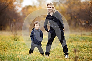 Young mother and son in autumn forest park, yellow foliage. Casual wear. Kid wearing blue jacket. Incomplete family