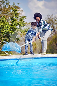 Young mother and son cleaning the pool with a cleaning net together standing by the pool, working as a team