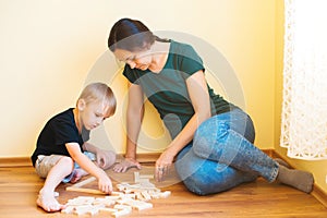 Young mother and son playing with wooden blocks indoor. Happy family spends time together at home.