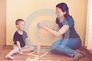 Young mother and son playing with wooden blocks indoor. Happy family spends time together at home.