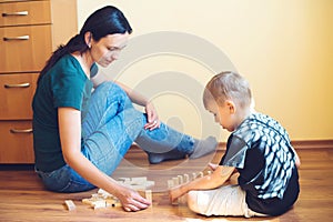 Young mother and son playing with wooden blocks indoor. Happy family spends time together at home.