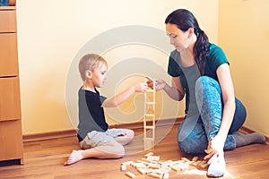 Young mother and son playing with wooden blocks indoor. Happy family spends time together at home.