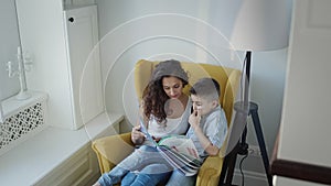 Young Mother And Son Read Book Together. Young Pretty Woman With Long Curly Hair Holding Book In Her Hands.