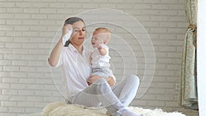 Young mother soothes a crying little baby at home in the bedroom. Close-up.