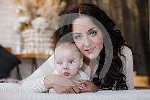 Young mother spends time with her newborn son, playing together, lying on a white bed in the bedroom