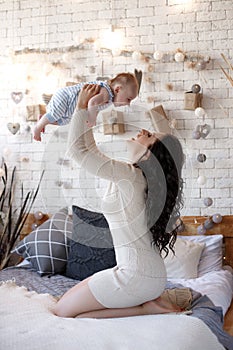 Young mother spends time with her newborn son, playing together, lying on a white bed in the bedroom