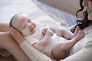 Young mother spends time with her newborn son, playing together, lying on a white bed in the bedroom