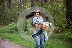 young mother is spinning with a baby in her arms. happy mom dancing with toddler on the background of nature and forest