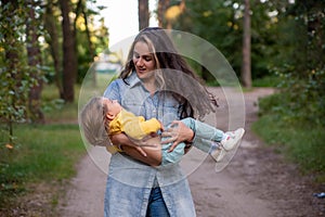 young mother is spinning with a baby in her arms. happy mom dancing with toddler on the background of nature and forest