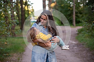 young mother is spinning with a baby in her arms. happy mom dancing with toddler on the background of nature and forest