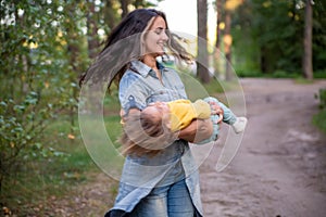 young mother is spinning with a baby in her arms. happy mom dancing with toddler on the background of nature and forest