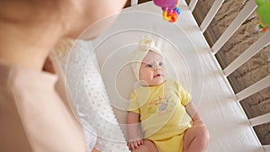 Young mother stands near bassinet and watches baby daughter