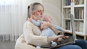 Young mother stroking her baby while working from home office on laptop. Concept of family happiness and child