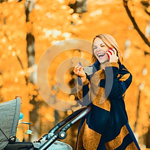 A young mother with a stroller is talking on her mobile phone while walking in the park