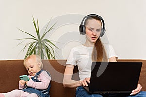 Young mother surf the Internet with laptop while small baby playing with phone. Irresponsible parents