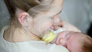 Young mother sway at  hands of  sleeping baby and gently kisses its cheek