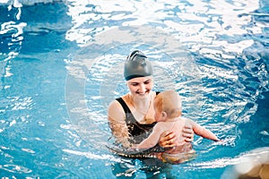 Young mother, swimming instructor and happy little girl in paddling pool. Teaches infant child to swim. Enjoy first day of