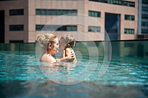 Young mother swimng with her little toddler daughter in the pool on the roof of a skyscraper in a metropolis