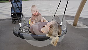 A young mother swings with her son on a swing. Mom and her son are swinging on a swing-nest in the courtyard of the