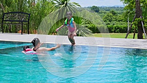 Young mother takes care of a daughter who is about to jump into the pool. Cute little sisters are enjoying swimming with her mom i