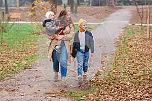 Young mother taking child to school, and baby son to kindegarden. Autumn time change. Parent, baby son, son schoolboy. Happy