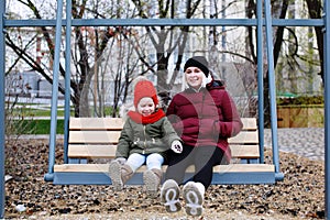 Young mother talking to her cute little daughter outdoors sitting together in warm clothes